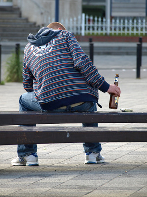 Jugenlicher mit einer Flasche Bier auf einer Parkbank